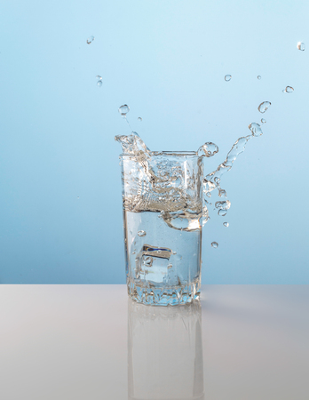 Splash from ice cube in a glass of water, on the nature blue backgroundの写真素材
