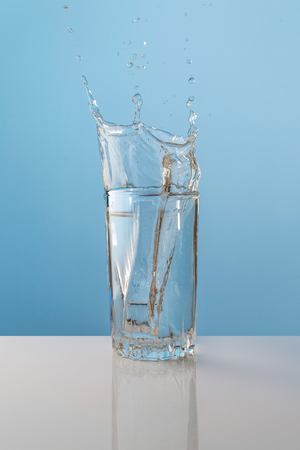 Splash from ice cube in a glass of water, on the nature blue backgroundの写真素材