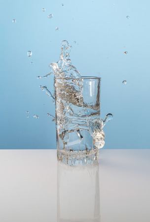 Splash from ice cube in a glass of water, on the nature blue backgroundの写真素材