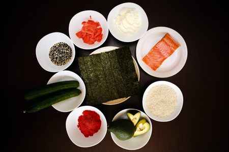 Table served with Ingredients of sushi in plates on dark background. rice with vegetables, nigiri, soy sauce, cucumber, salmon, avocado, caviar, nori, sesame. Before to be a roll. Top viewの写真素材