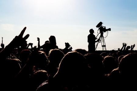 silhouette of cameraman operator shooting a live rock concert, fans around raised handsの写真素材