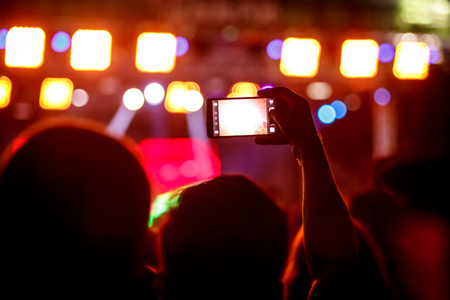 Boy makes photo with His smartphone to a concert to share the moment with friends on social networks, image with copyspace, added vintage effect, blurred effect and grainの写真素材