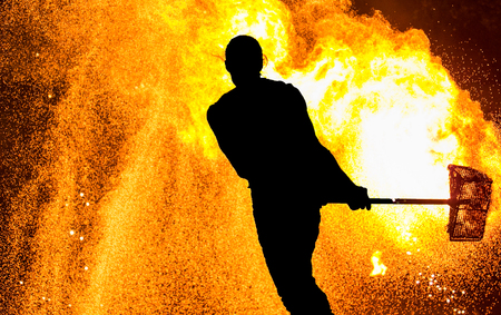 Fireshow performance. Silhouette of man with hammer, fire aroundの写真素材