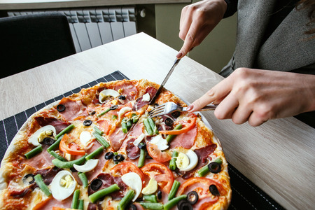 woman hands Slicing fresh pizza with beans, cheese, ham, eggs, pepperoni and vegetables. Cutting pizzaの写真素材