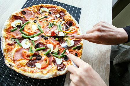woman hands Slicing fresh pizza with beans, cheese, ham, eggs, pepperoni and vegetables. Cutting pizzaの写真素材