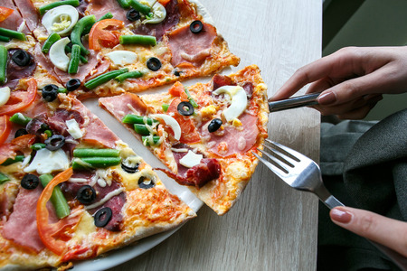 woman hands Slicing fresh pizza with beans, cheese, ham, eggs, pepperoni and vegetables. Cutting pizzaの写真素材