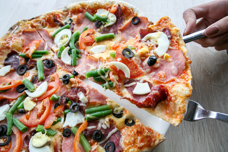 woman hands Slicing fresh pizza with beans, cheese, ham, eggs, pepperoni and vegetables. Cutting pizzaの写真素材