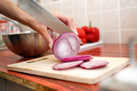 Woman's hand cut red onions on cutting board in home kitchenの写真素材