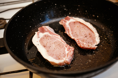 Raw uncooked pork meat steaks with spices in a frying pan, cooking food at home kitchenの写真素材