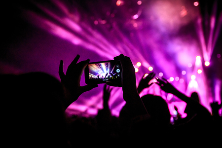 Hand with a smartphone records live music festival, Taking photo of concert stage, live concert, music festival, happy youth, luxury party, landscape exterior - purple lightの写真素材