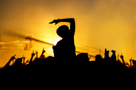 Young girl enjoys a rock concert, Silhouette on sunset, hands up on openairの写真素材
