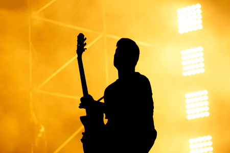Silhouette of guitar player, guitarist perform on concert stage. Orange background, smoke, concert spotlights.の写真素材