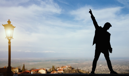 Silhouette of a standing man with raised up arms on the top. Rock star pose. Down town and mountains in the backgroundの写真素材