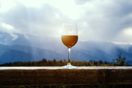 Red wine glass at a picnic standing on a wooden table in front of beautiful mountain background.の写真素材