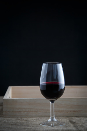 a glass of red wine on black background, cloth stand at the bottom, wooden tray behindの写真素材