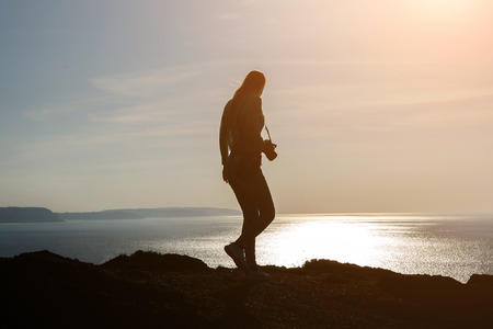 Silhouette Woman Photographing Landscape At Sunset. Female photographer holding a camera.の写真素材