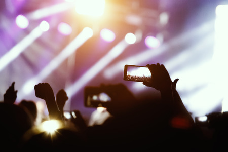 Silhouette of hands using camera phone to take pictures and videos at live concert, smartphone...
