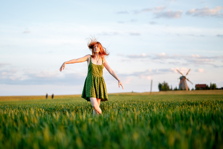 The girl dances in the green field. Summer. Mill on hamlet in the background.の写真素材