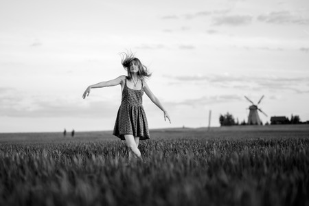The girl dances in the green field. Summer. Mill on hamlet in the background. Monochromeの写真素材
