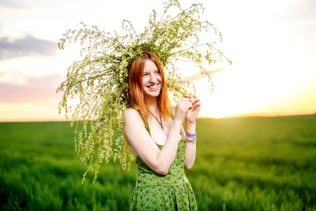 Beautiful girl in a green dress with wreath of flowers lay. Green meadow on sunsetの写真素材