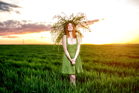 Beautiful girl in a green dress with wreath of flowers lay. Green meadow on sunsetの写真素材