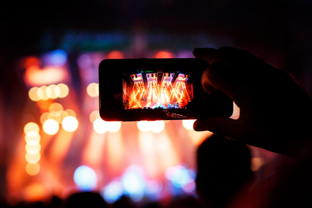 Hand with a smartphone records live music festival and taking photo of concert stage
