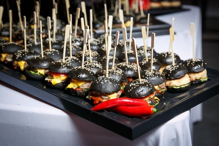 A lot of small black burgers on event catering, snacks on tableの写真素材