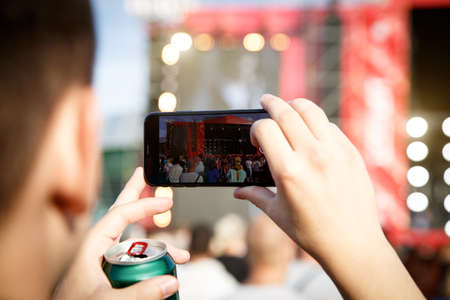 Man holding smartphones in hands and photographing. Taking photo on summer outdoor music concert festival.の写真素材