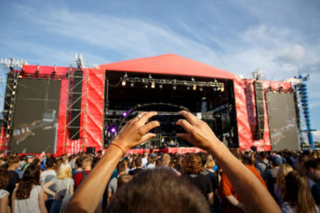 Man holding smartphones in hands and photographing. Taking photo on big summer outdoor music concert festival.の写真素材
