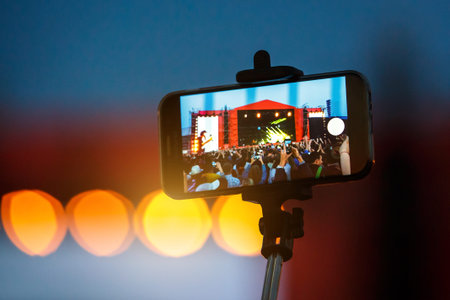 Smartphone on selfie monopod stick. Concert background