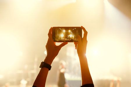 Soft focus colorful background of hand holding smartphone, Recording a concert with mobile phone,...