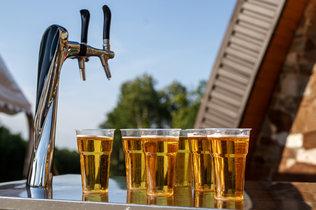 A row of plastic beer glasses with a lager beer on outdoor partyの写真素材