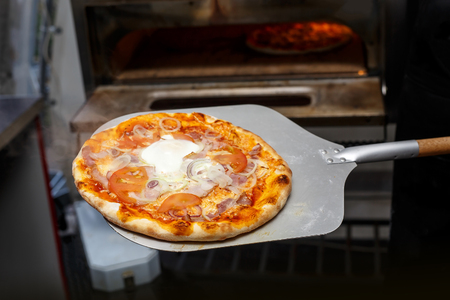 Putting pizza in oven at restaurant kitchenの写真素材