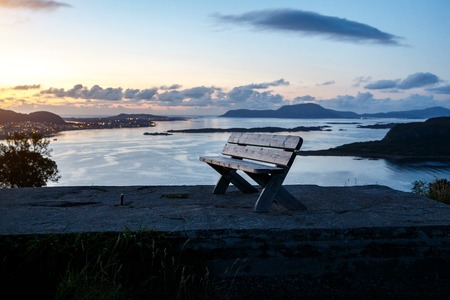 A lone wooden bench stands on top of a mountain. Sunset evening timeの写真素材