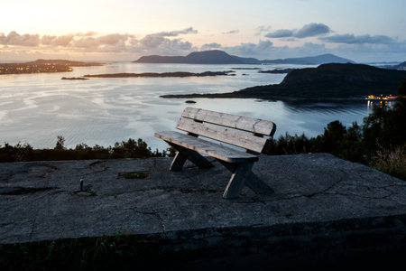 A lone wooden bench stands on top of a mountain. Sunset evening time