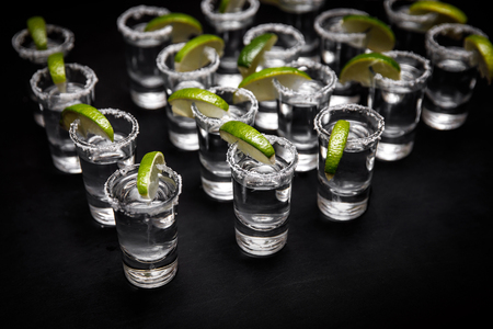 Tequila shots with lime and sea salt on black tableの写真素材