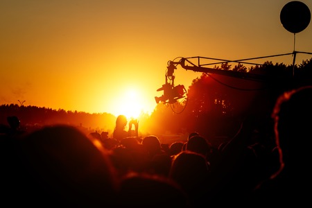 Video camera live television on summer event. Silhouette, outside studio against orange sunset skyの写真素材