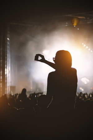 Silhouette of the girl with smartphone gets pleasure from the rock concert