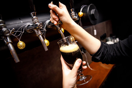 Female bartender hands pouring dark beer from the tap in bar.の写真素材