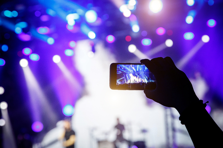 Filming a concert on mobile phone camera, blue light of stageの写真素材