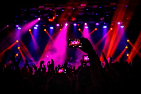 Smartphone in hand at a concert, purple light from stage.の写真素材