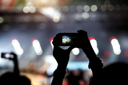 A mobile phone in the hands of fan at summer music show. Recording concertの写真素材
