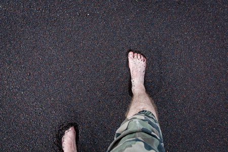 Men's feet are on the volcanic black sand.の写真素材