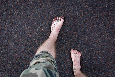 Men's feet are on the volcanic black sand.の写真素材