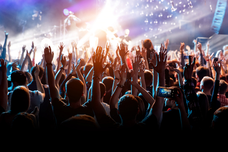 A man with his hands up at a concert of his favorite group. Light from the stageの写真素材