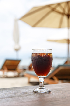 Tulip glass with cola on table. Beach umbrellas on the backgroundの写真素材