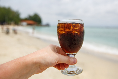 Cooling drink in hand on beach.の写真素材