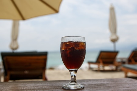 Cola glass on beach with umbrellas. Cooling drink on summer.の写真素材