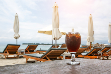 Cola glass on beach with umbrellas. Cooling drink on summer.の写真素材