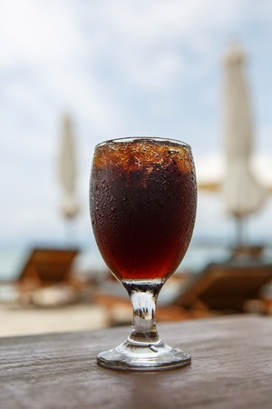 Tulip glass with cola on table. Beach umbrellas on the backgroundの写真素材